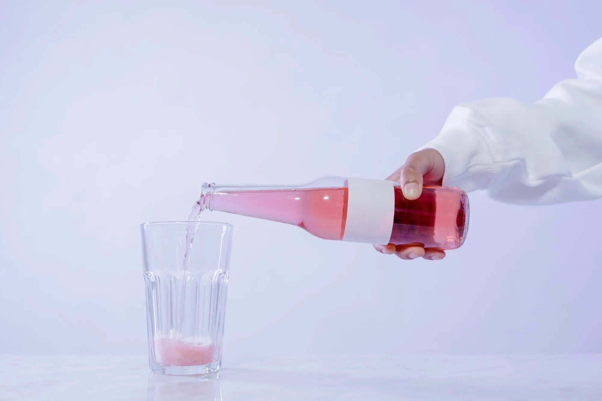 Pink collagen drink poured from a bottle into a glass