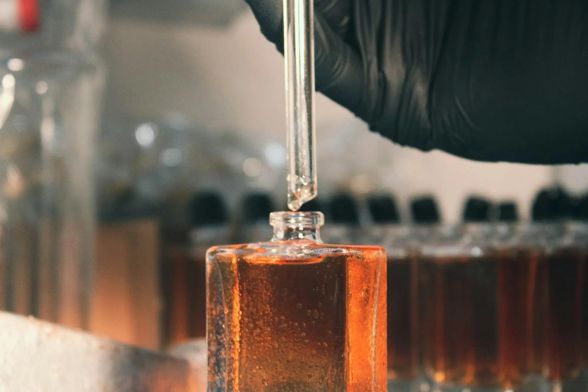 A dropper releasing amber liquid into a glass bottle in a lab